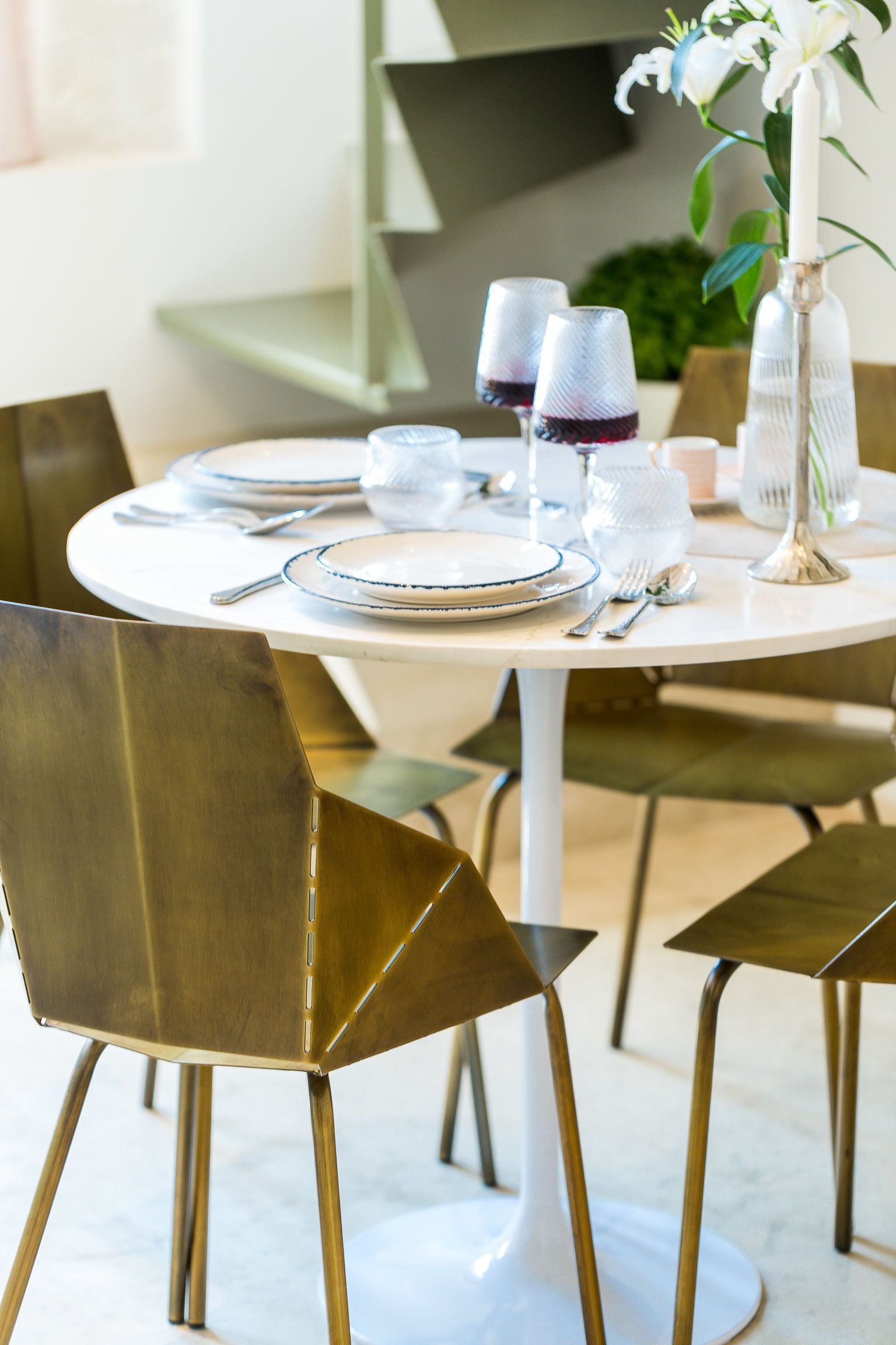 Una mesa de comedor dispuesta con platos, vasos y cubiertos, rodeada de sillas modernas.
