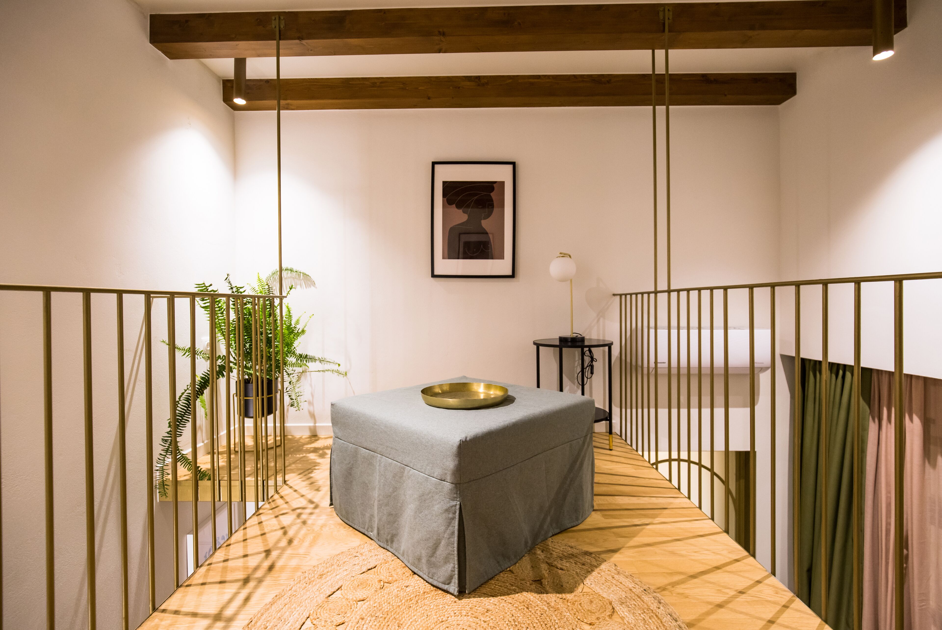 A modern, minimalist room with a grey ottoman, a framed artwork on the wall, and a potted plant.