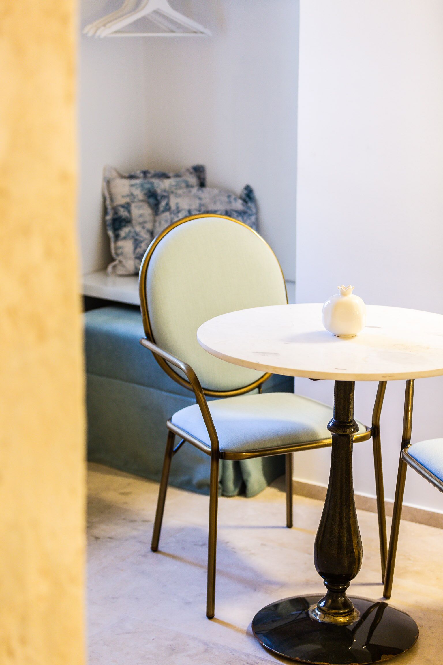A round table with a white top and a single white object on it, a chair with a light green upholstered seat and backrest, and a dark wooden base.