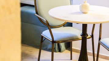 Une table ronde avec un plateau blanc et un seul objet blanc posé dessus, une chaise avec un siège et un dossier rembourrés de couleur vert clair, et un pied en bois foncé.