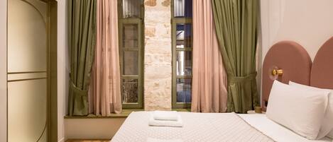 A hotel room with a bed, two towels, a stone wall, and a window with curtains.