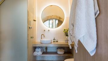 A modern bathroom with a round mirror, a sink, and a toilet. There are towels and a basket on the counter.