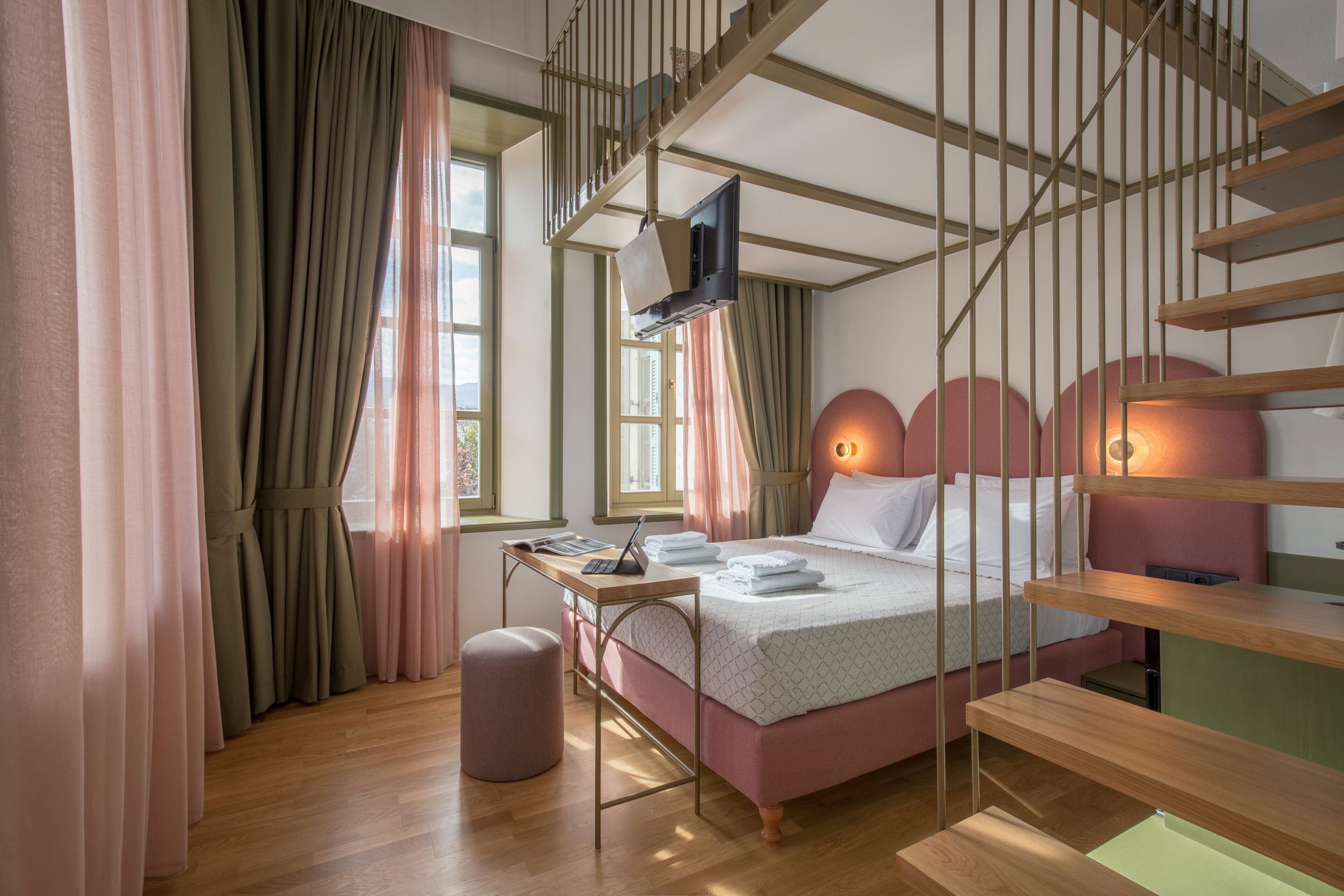 Een moderne slaapkamer met een bed, een bureau, een stoel, een klein krukje, een televisie en een trap.