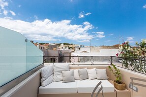 A rooftop terrace with a white sofa, a wicker plant, and a clear view of the cityscape. - Neratze Hammam Suites (Rethymno)