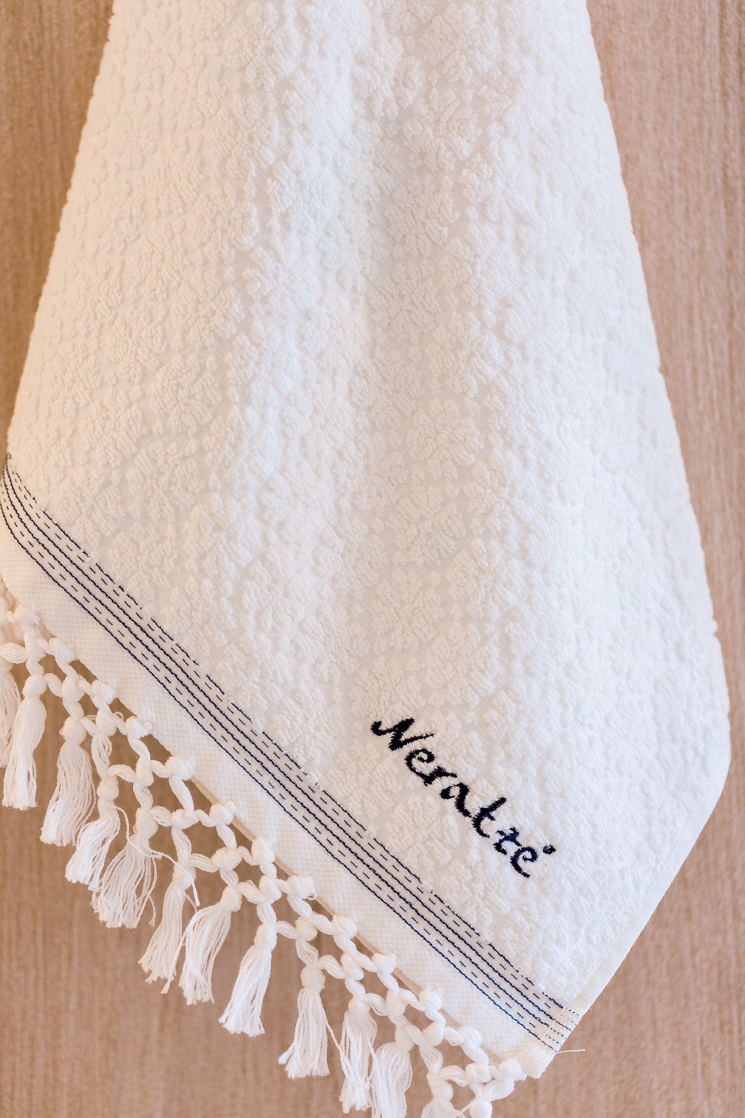 Una toalla blanca con flecos y texto bordado.