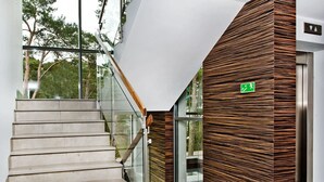 A modern staircase with glass railings, a wooden panel wall, and a green exit sign. - Villa Aqua BlueApart Jurata (Jurata)