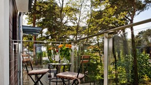 A glass-enclosed patio with two chairs and a table, surrounded by lush greenery and trees. - Villa Aqua BlueApart Jurata (Jurata)