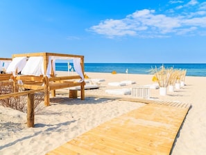 Escena de playa con estructuras de madera, toldos blancos y sillas de descanso.