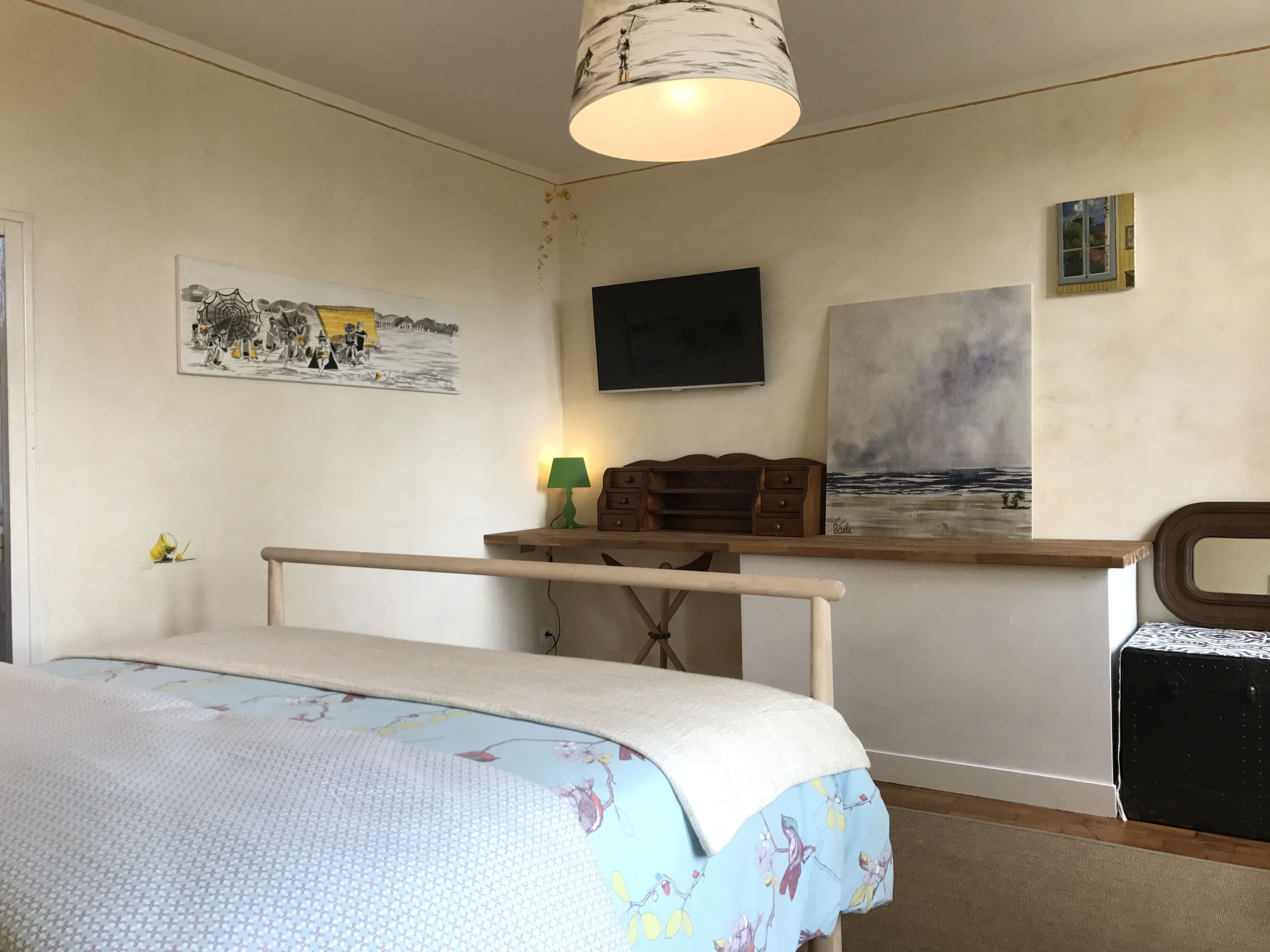 Un dormitorio con cama, un escritorio con lámpara, televisión y obras de arte en las paredes.