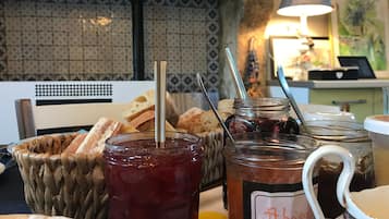 A table with jars of jam and bread, a basket, and a lamp in a room with patterned tiles.