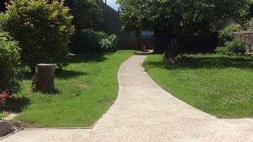Un sendero pavimentado que atraviesa un jardín con árboles y arbustos.