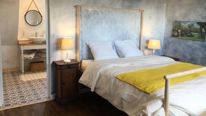 A bedroom with a bed, two bedside lamps, a nightstand, a wooden cabinet, a mirror, and a painting on the wall. - L'Ermitage (Saint-Vaast-la-Hougue)