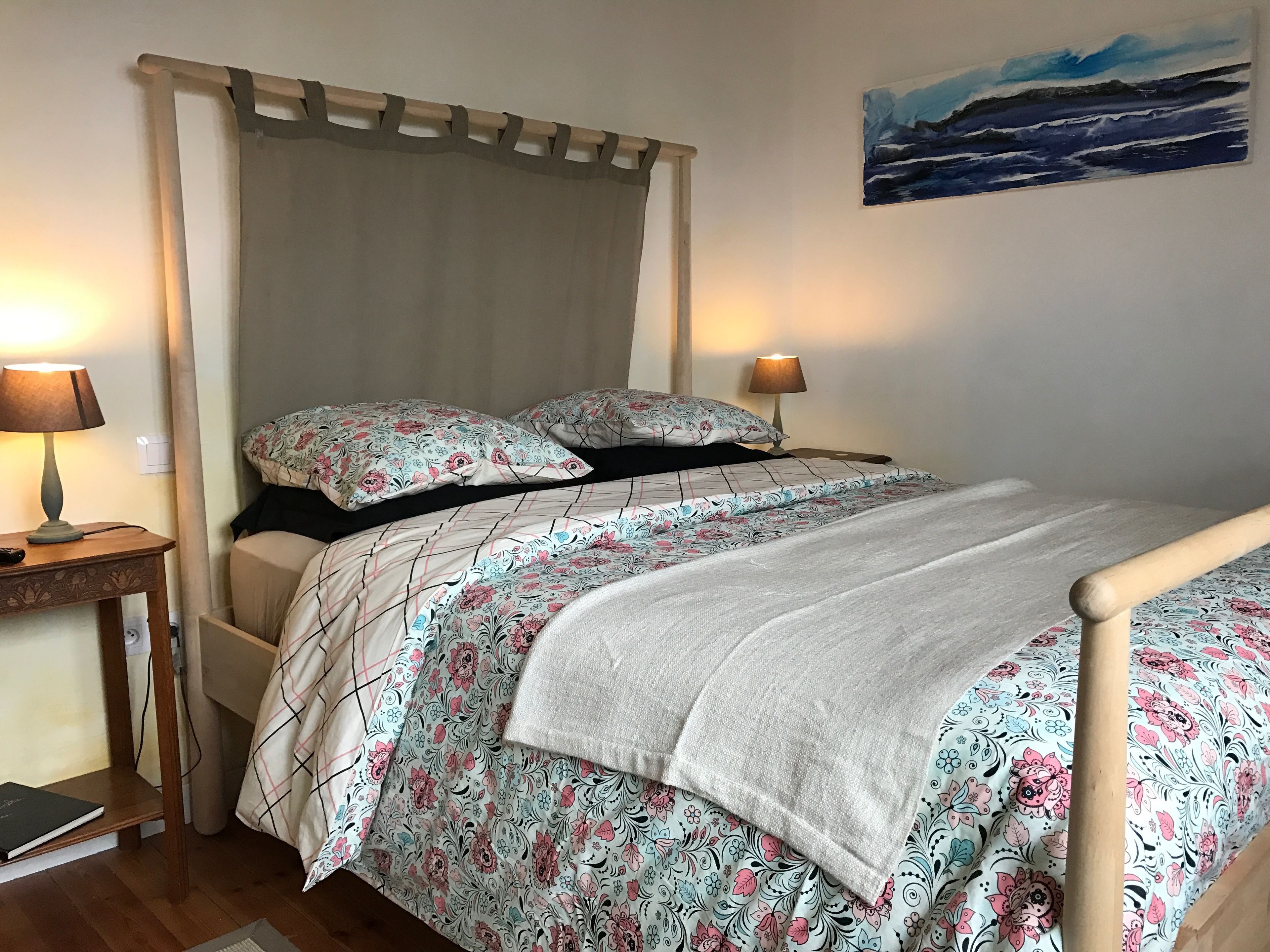 Een slaapkamer met een bed, twee bedlampen, een nachtkastje, een houten stoel en een schilderij aan de muur.