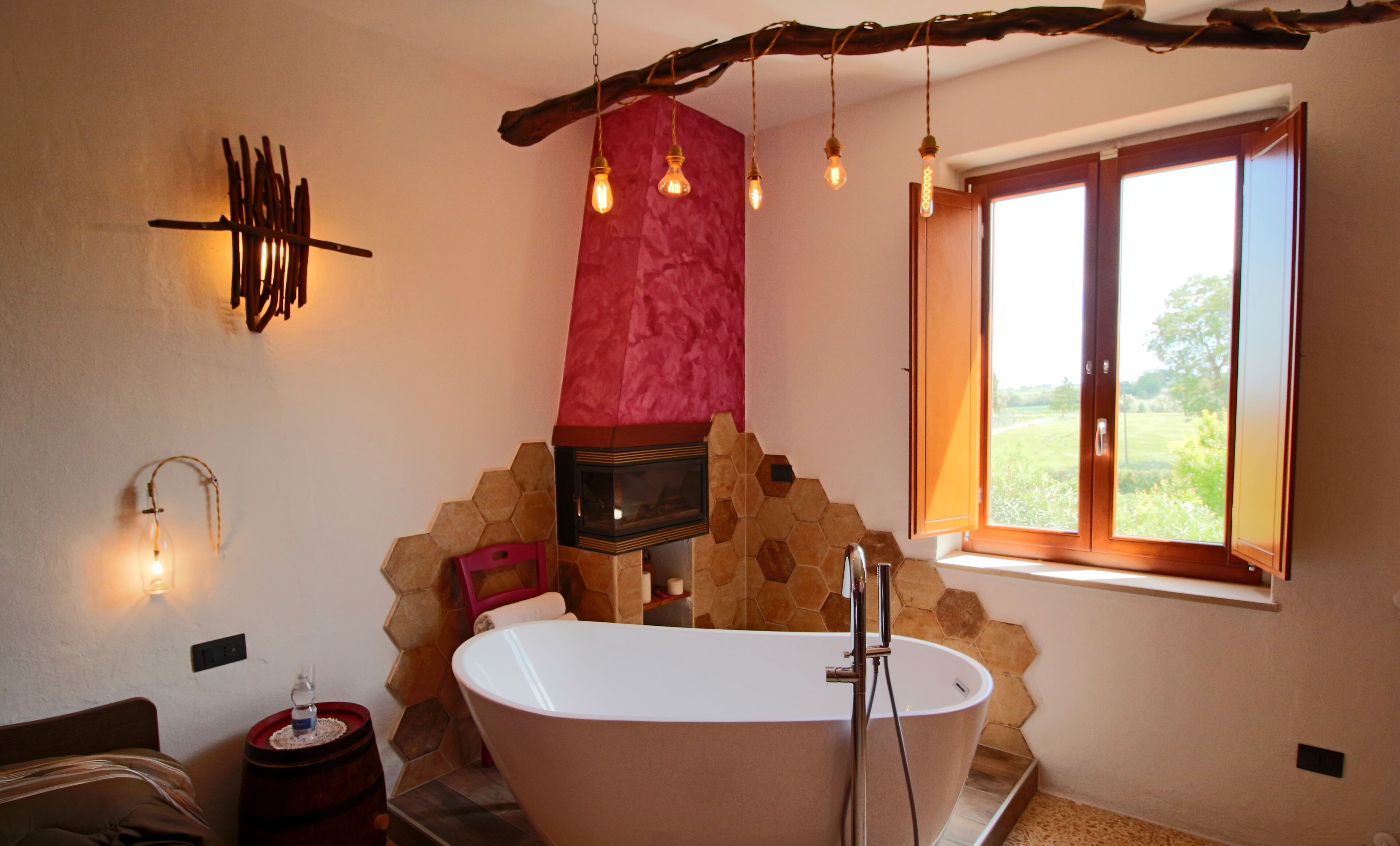 A modern bathroom with a freestanding bathtub, a red accent wall, and a window with a view of greenery.