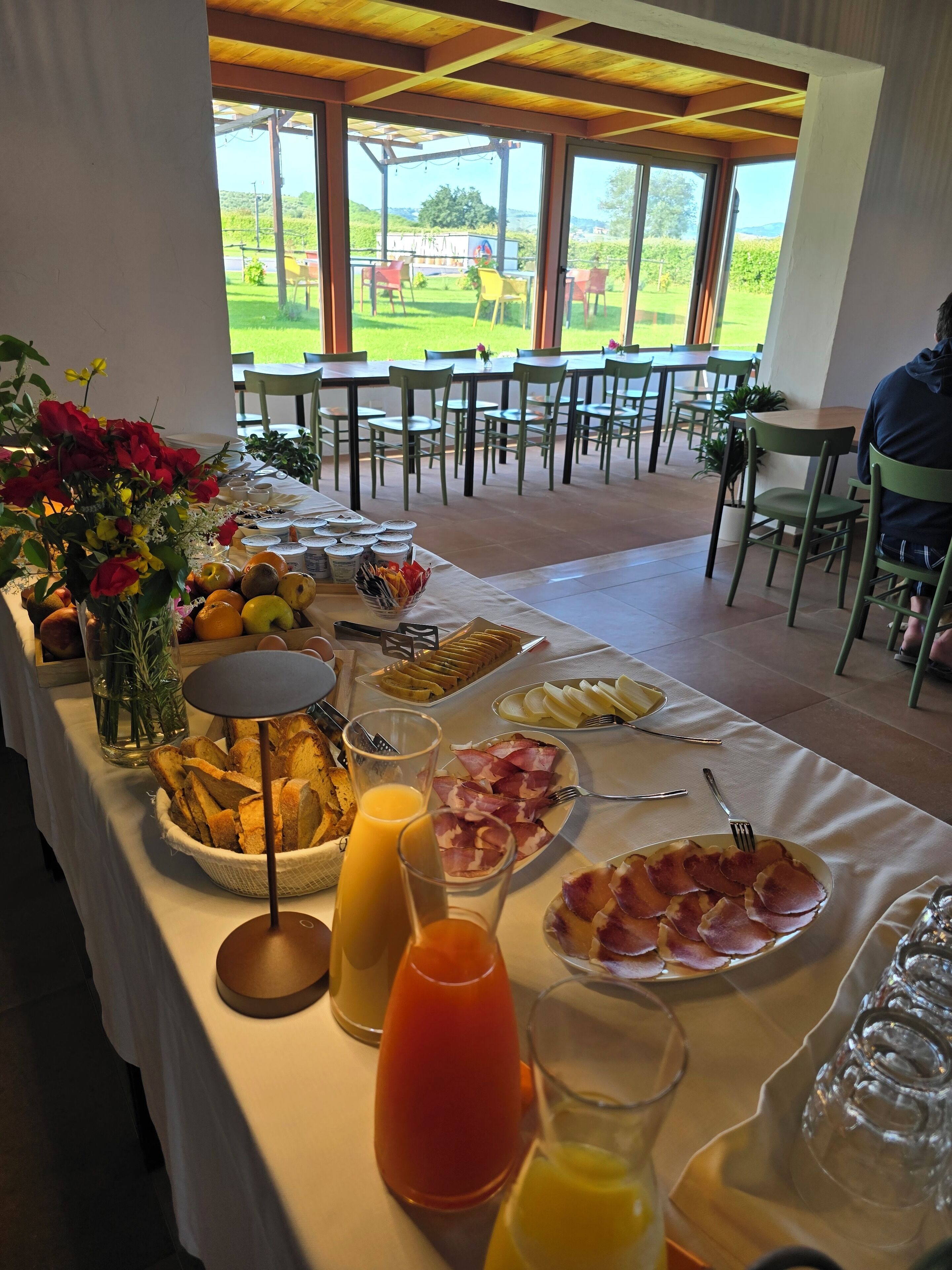 A breakfast buffet with various food items and drinks, set in a spacious dining area with a view of a green landscape.