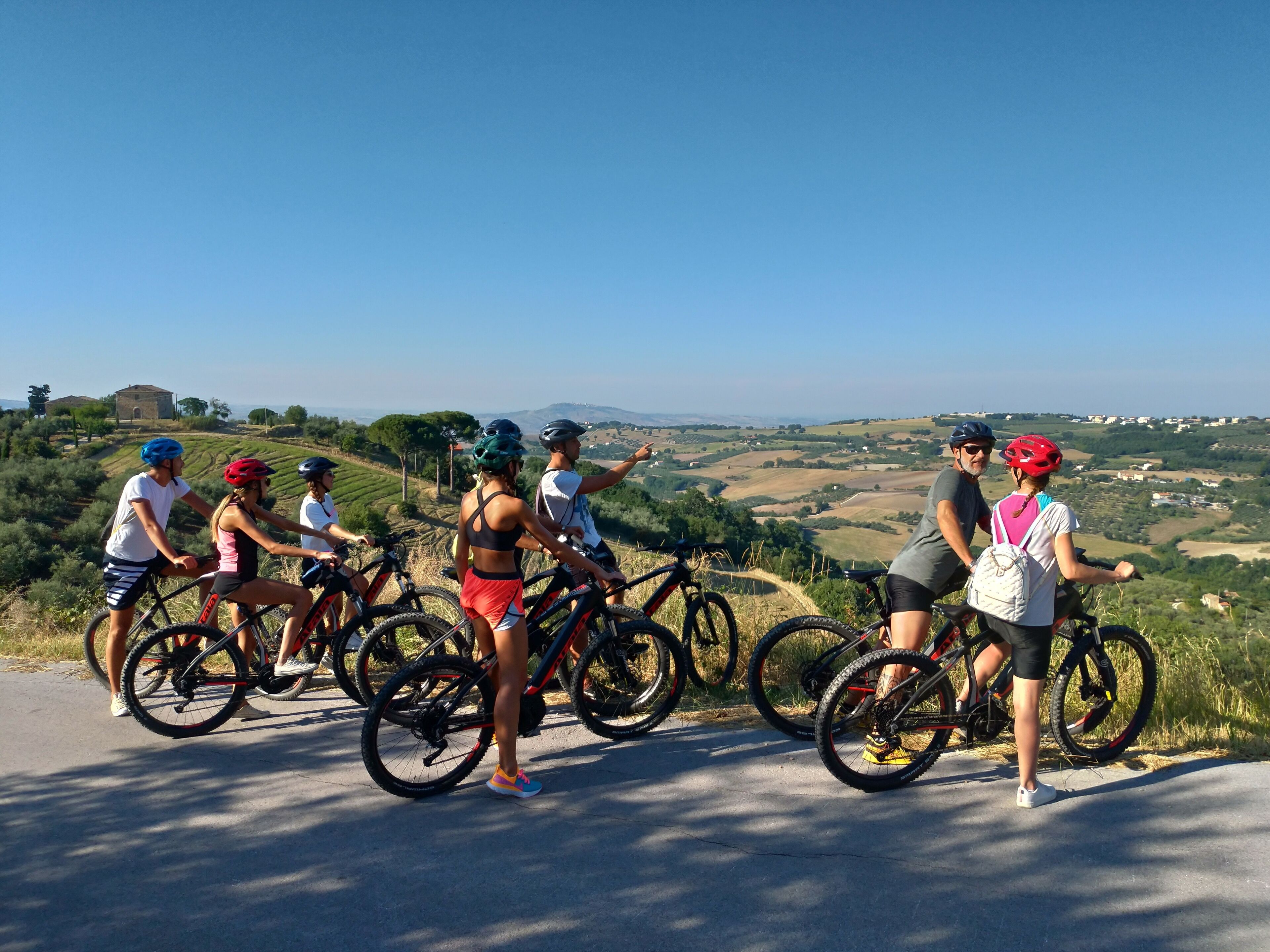 Un grupo de ciclistas en un camino pavimentado con vistas panorámicas de colinas ondulantes y un cielo despejado.