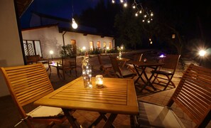 An outdoor patio with wooden tables and chairs, string lights, and candles.
