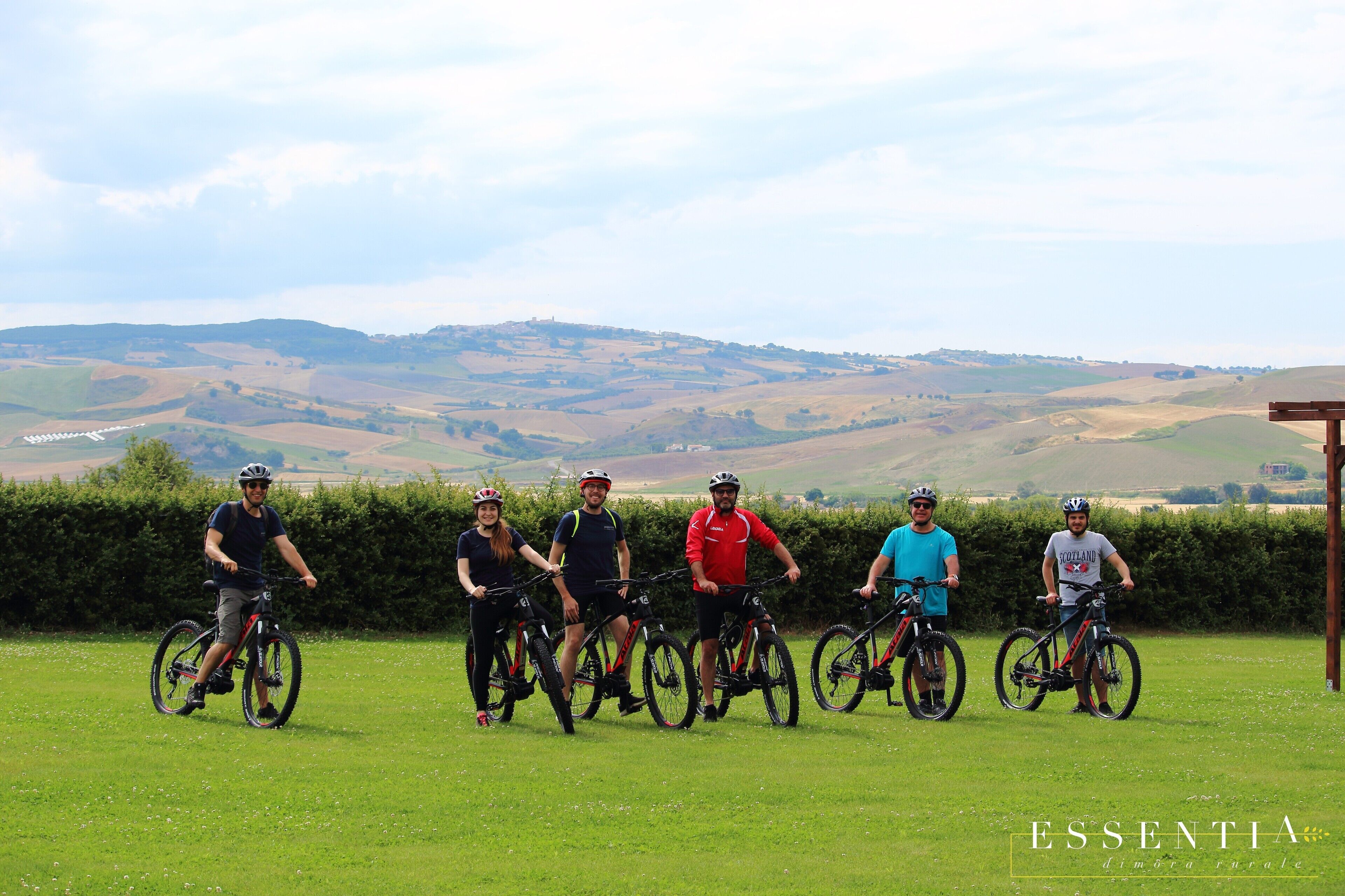 Un groupe de personnes à vélo se trouve dans un champ herbeux, avec un paysage vallonné en arrière-plan.