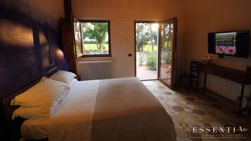 Ein Schlafzimmer mit Bett, Heizkörper, Fernseher und Blick ins Freie.