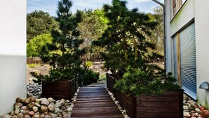 A wooden pathway leading to a house with a garage, surrounded by a garden with various plants and trees. - BlueApart Nadmorski Park Jastarnia (Jastarnia)