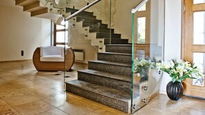 A modern staircase with glass railings, a white chair, and a vase of flowers. - BlueApart Nadmorski Park Jastarnia (Jastarnia)