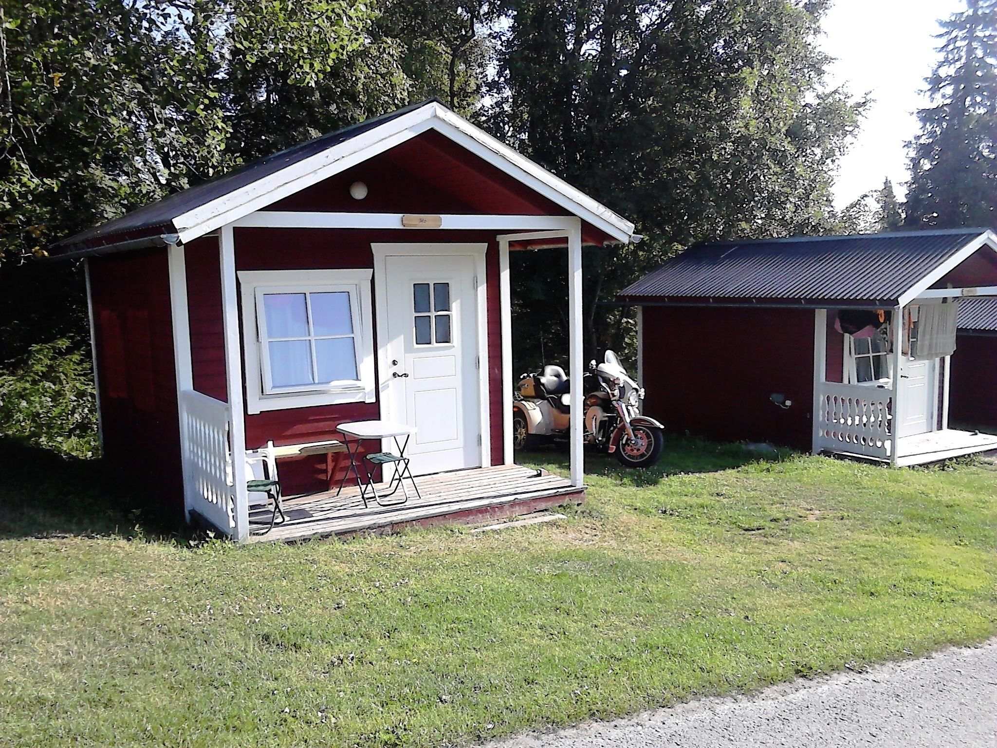 A small red cabin with a porch, a motorcycle, and a small table and chair.