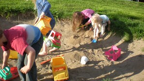 Niños jugando con arena y vehículos de juguete en una colina cubierta de césped.