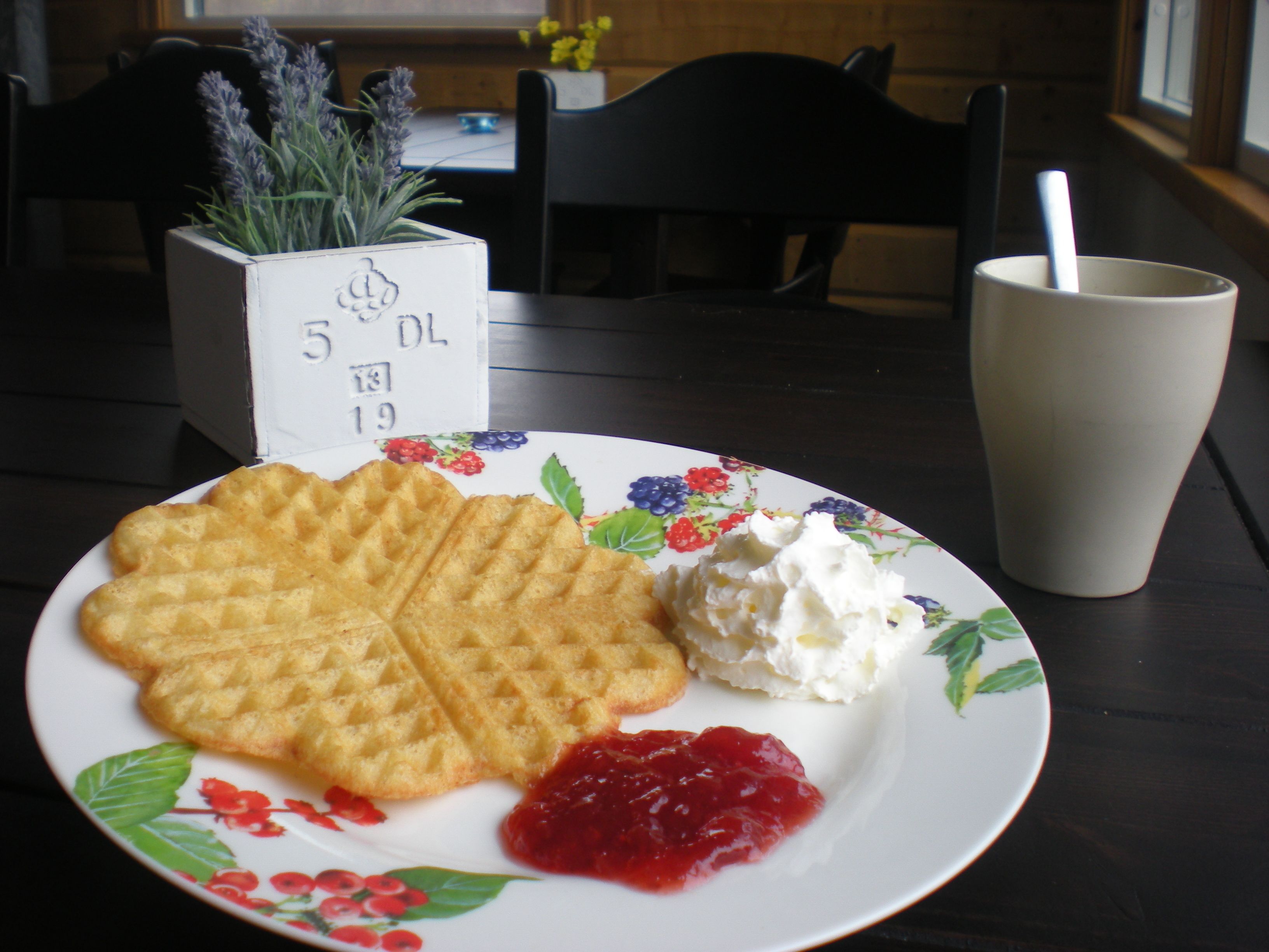 A plate with waffles, whipped cream, and jam on a floral plate.