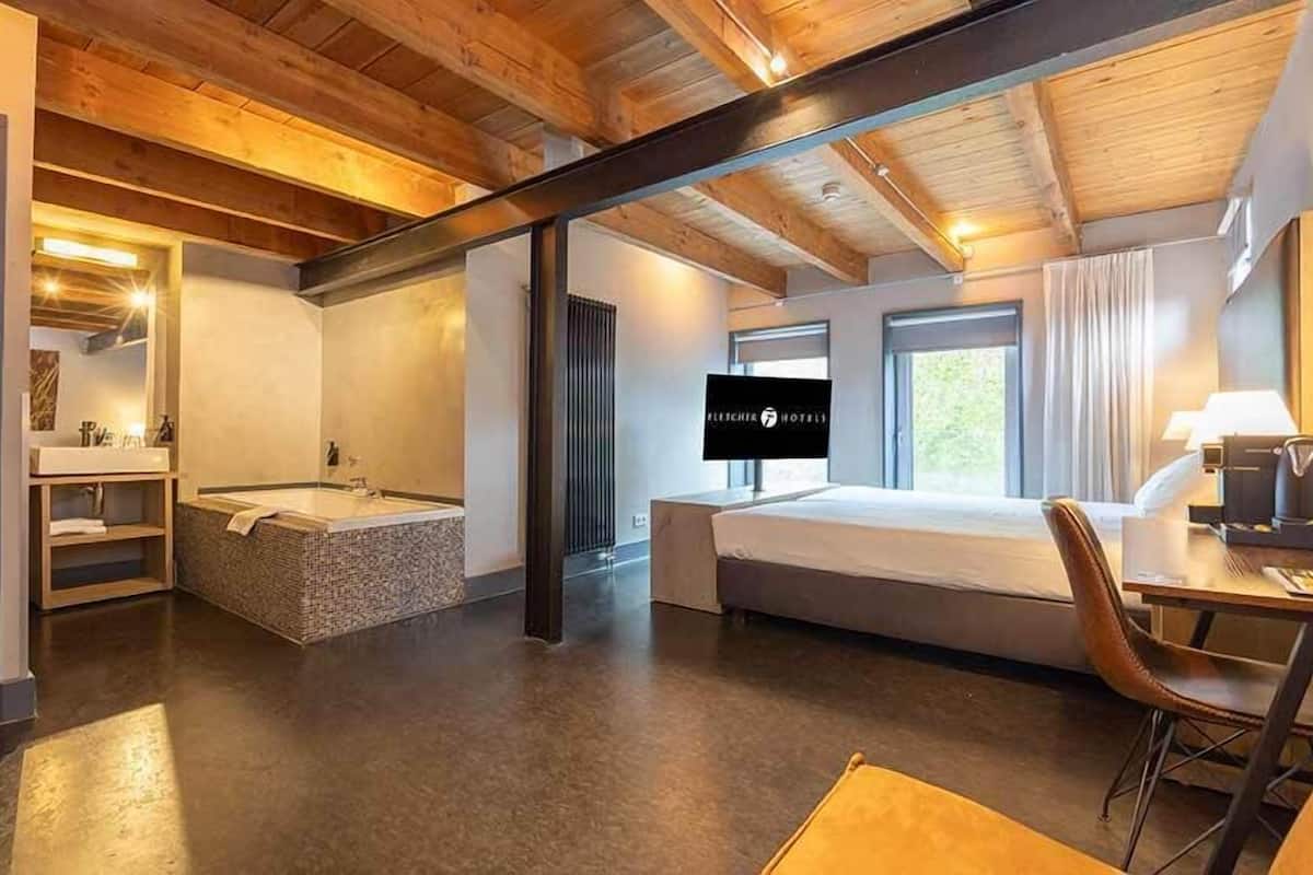 Une chambre d’hôtel moderne dotée d’un grand lit, d’une salle de bain séparée avec baignoire, d’un bureau avec une chaise et d’une télévision.