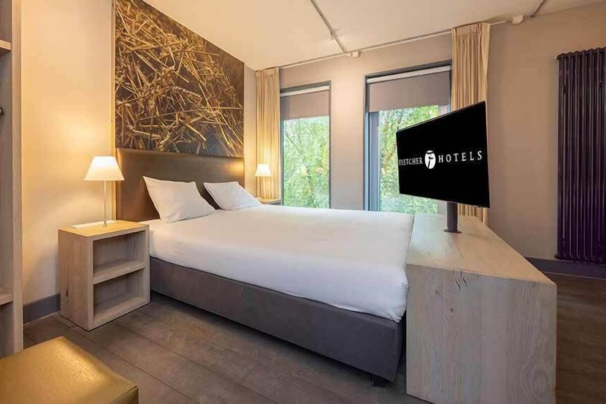 Une chambre d’hôtel avec un lit, deux tables de chevet, une télévision, un ventilateur et une vue sur la verdure.