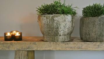 A rustic wooden shelf with two potted plants and two lit candles.