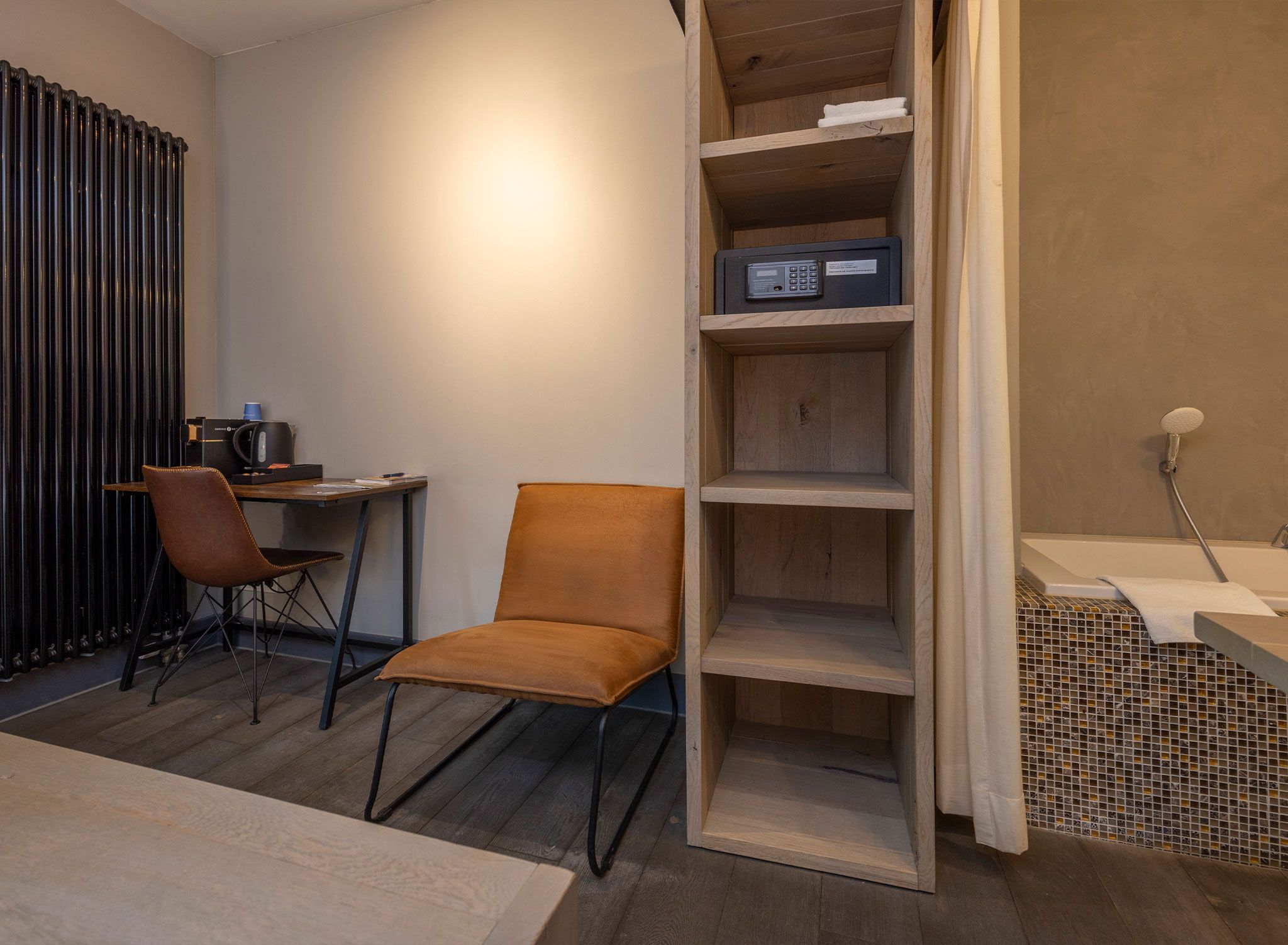 A room with a desk, two chairs, a radiator, a shelf with a radio, and a tiled shower area.
