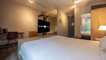 Una habitació d'hotel amb un llit gran, un escriptori amb una cadira, una televisió i una finestra que ofereix vistes a vegetació.