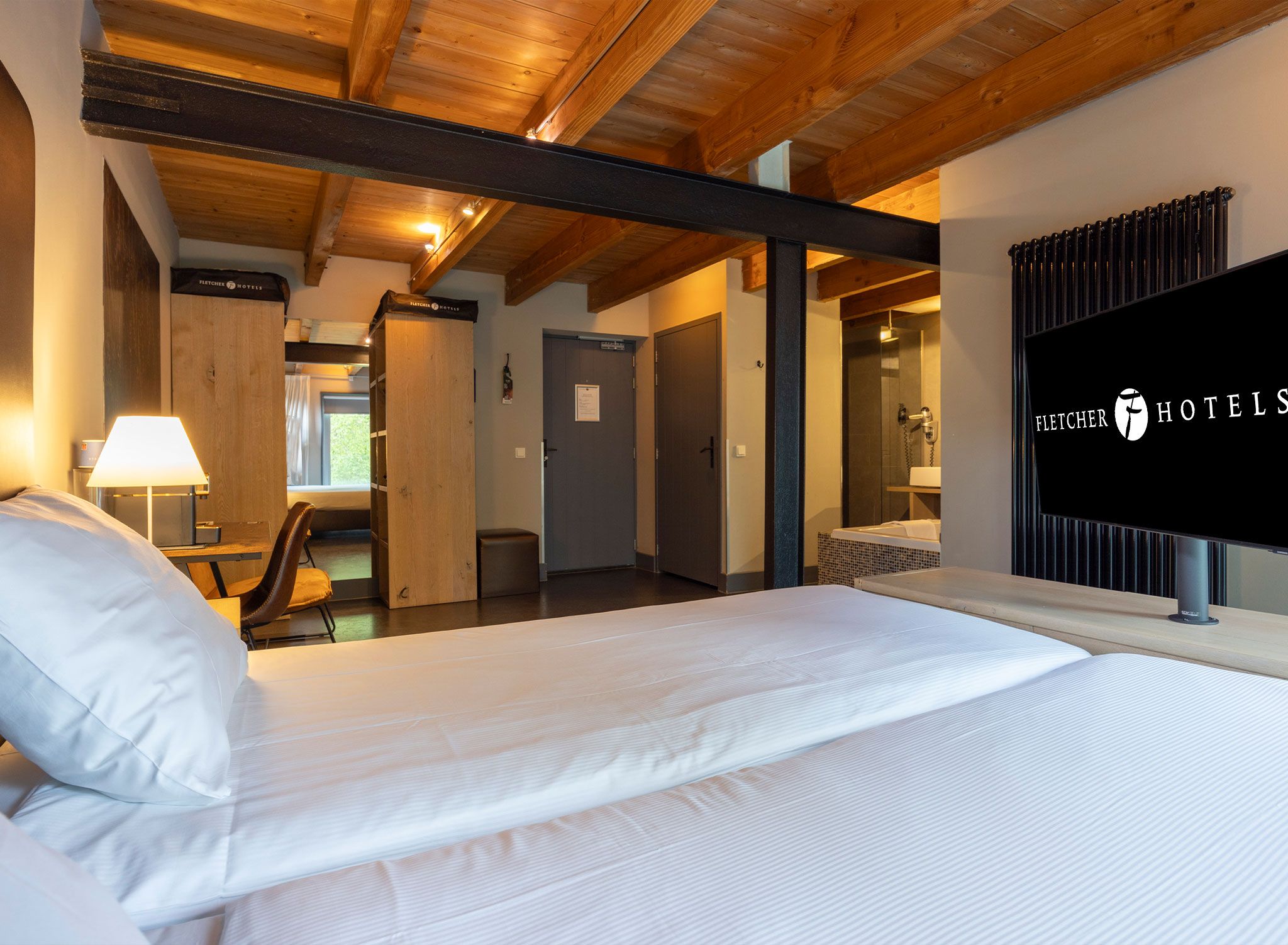 A hotel room with a bed, a desk, a chair, a lamp, and a shower area.