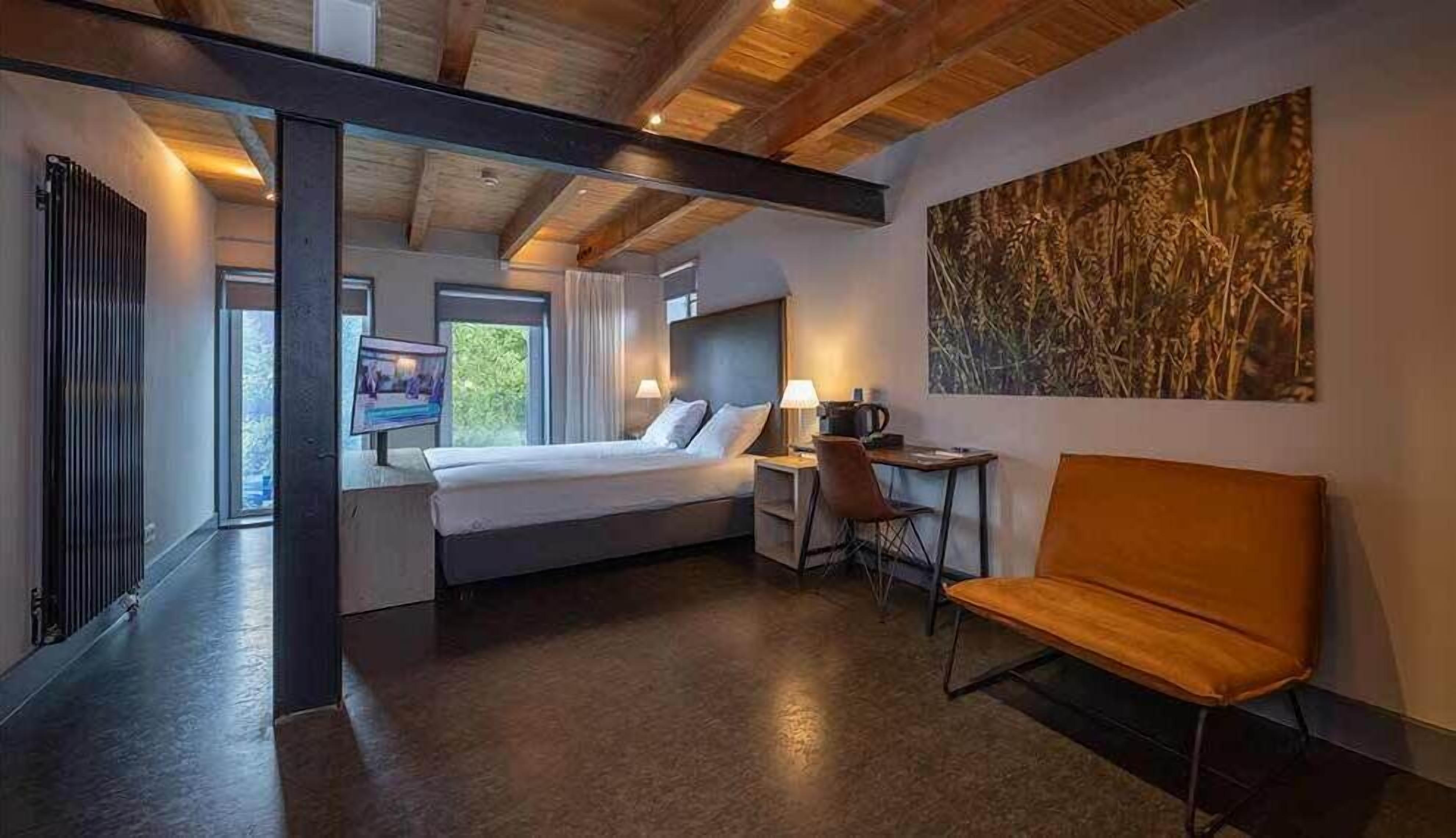 A modern hotel room with a bed, a desk, a chair, and a large window.