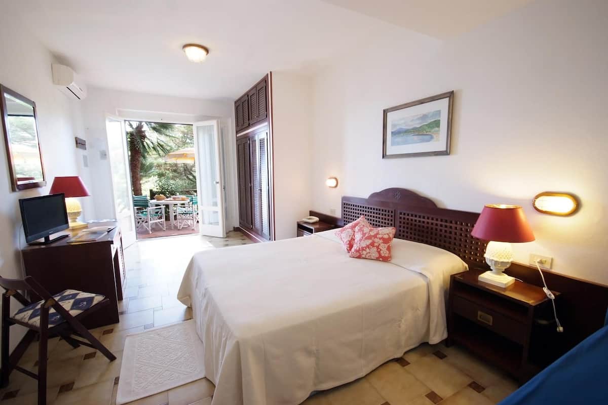 A hotel room with a bed, bedside lamps, a desk with a computer, a chair, and a view of the outdoors.