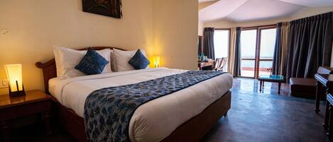 A spacious bedroom with a large bed, a wooden nightstand, a desk, and a balcony with curtains.
