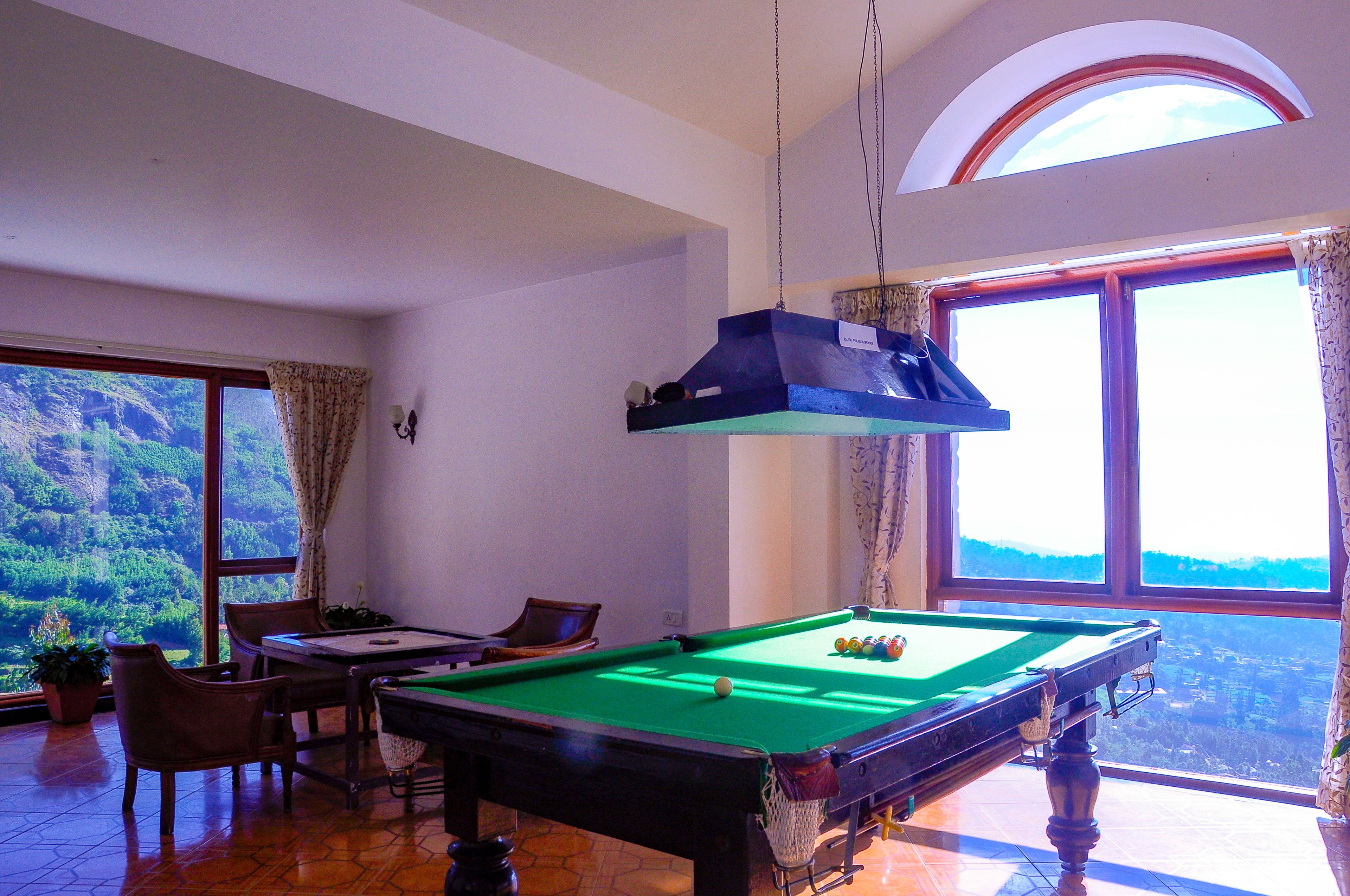 A pool table in a room with large windows and a view of a forest.