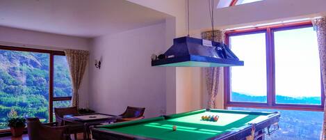 A pool table in a room with large windows and a view of a forest.