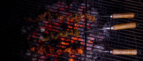 Una parrilla con brochetas de carne y verduras sobre fuego vivo.