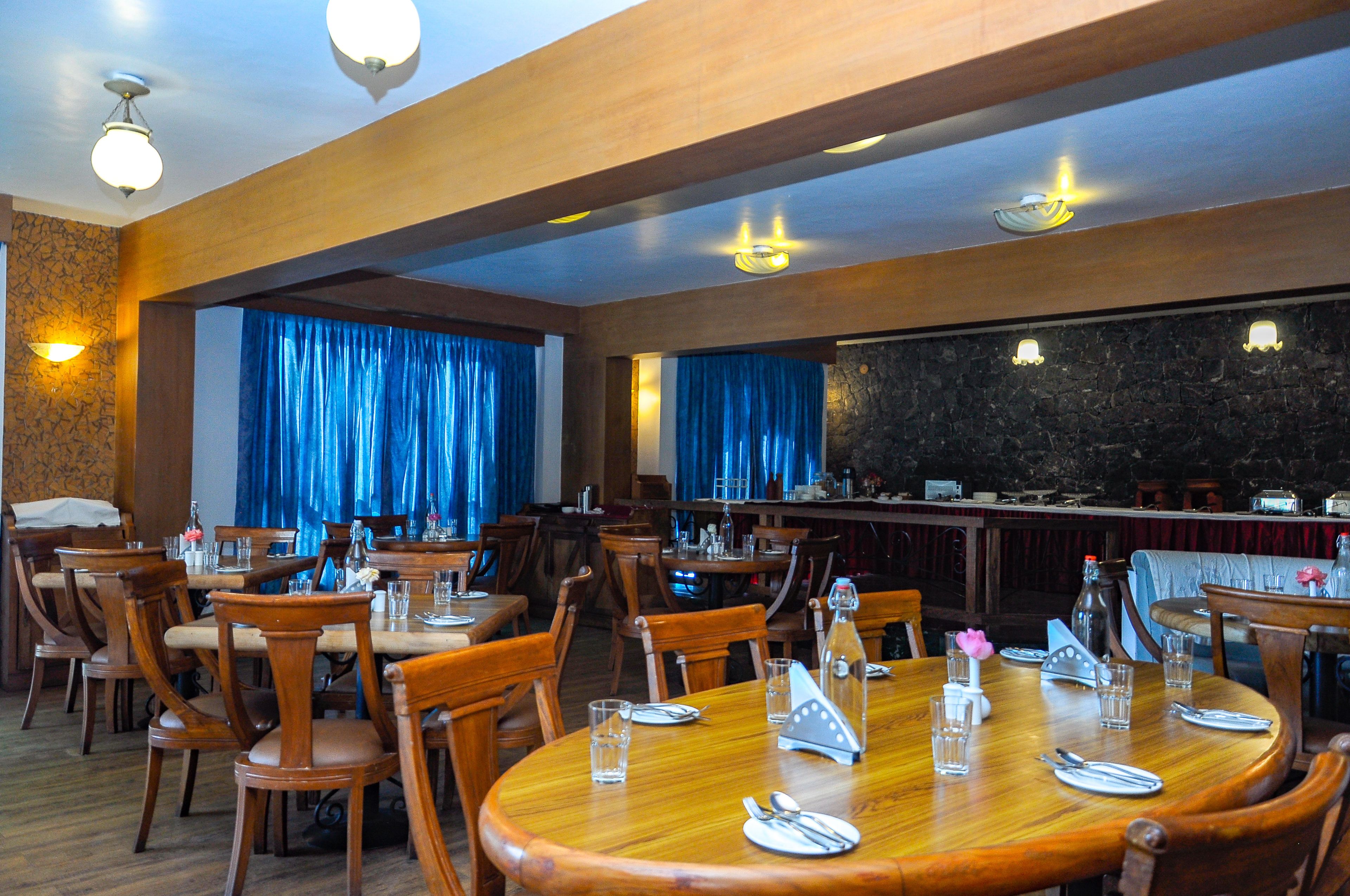 Un restaurante con mesas y sillas de madera, una zona de bar y cortinas azules.