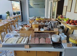 A buffet setup with various food items and condiments, including fruits, meats, and dairy products, arranged on a counter with labels. - COCO-MAT Athens Jumelle (Athens)