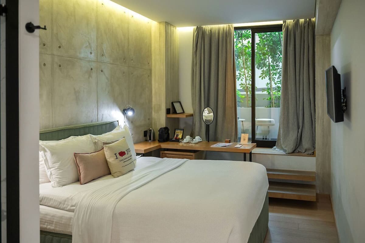 Quarto de hotel moderno com cama, mesa de cabeceira e janela com cortinas.