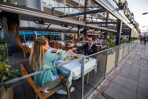 An outdoor dining area with tables and chairs, overlooking a street with buildings and pedestrians. - Izmir Palas Otel (Izmir)