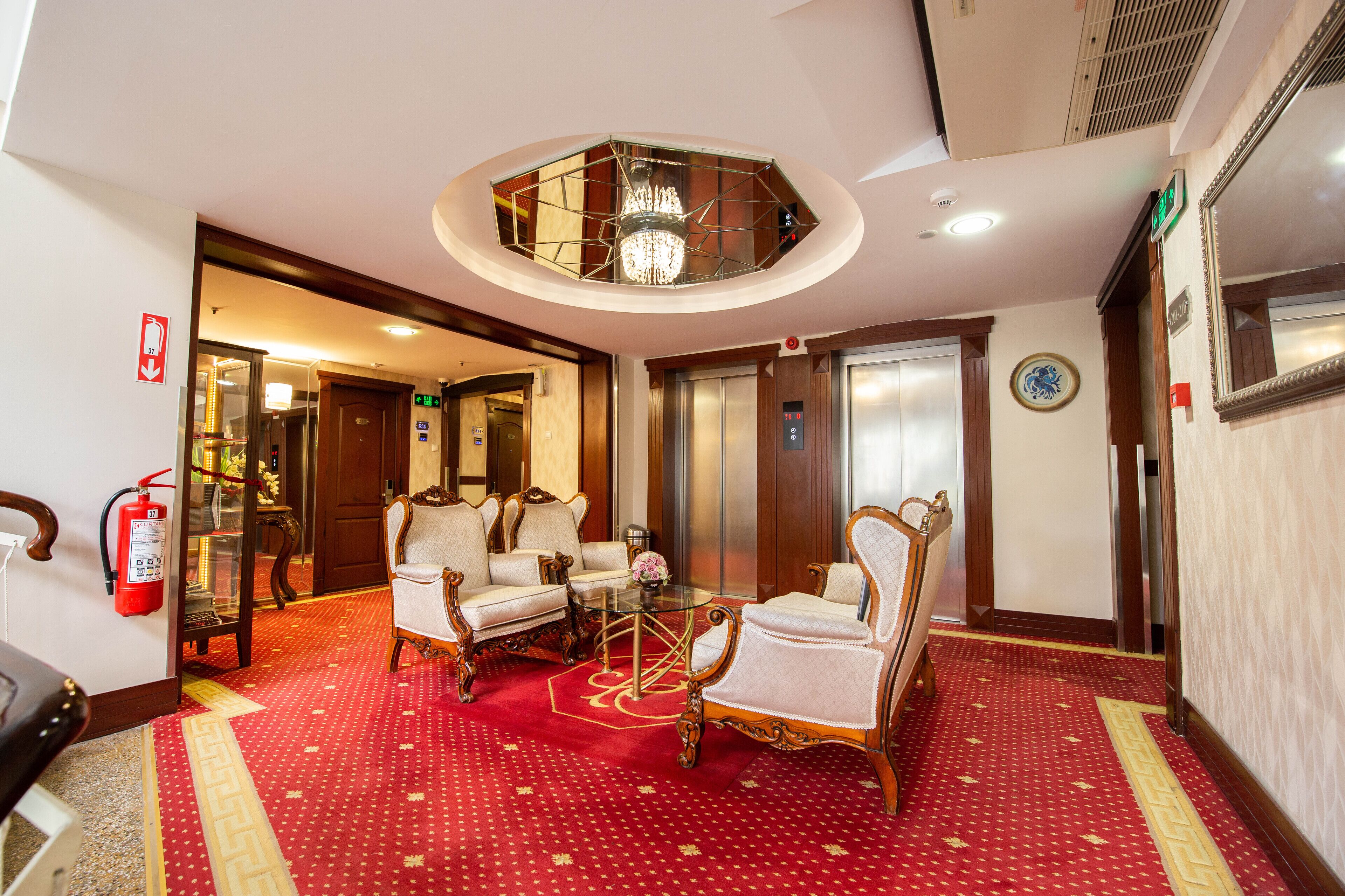 A hotel lobby with a red carpet, a chandelier, and a seating area with ornate chairs.