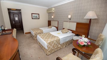 Habitación de hotel con dos camas individuales, un escritorio, una silla, una mesa con un arreglo floral y una puerta.
