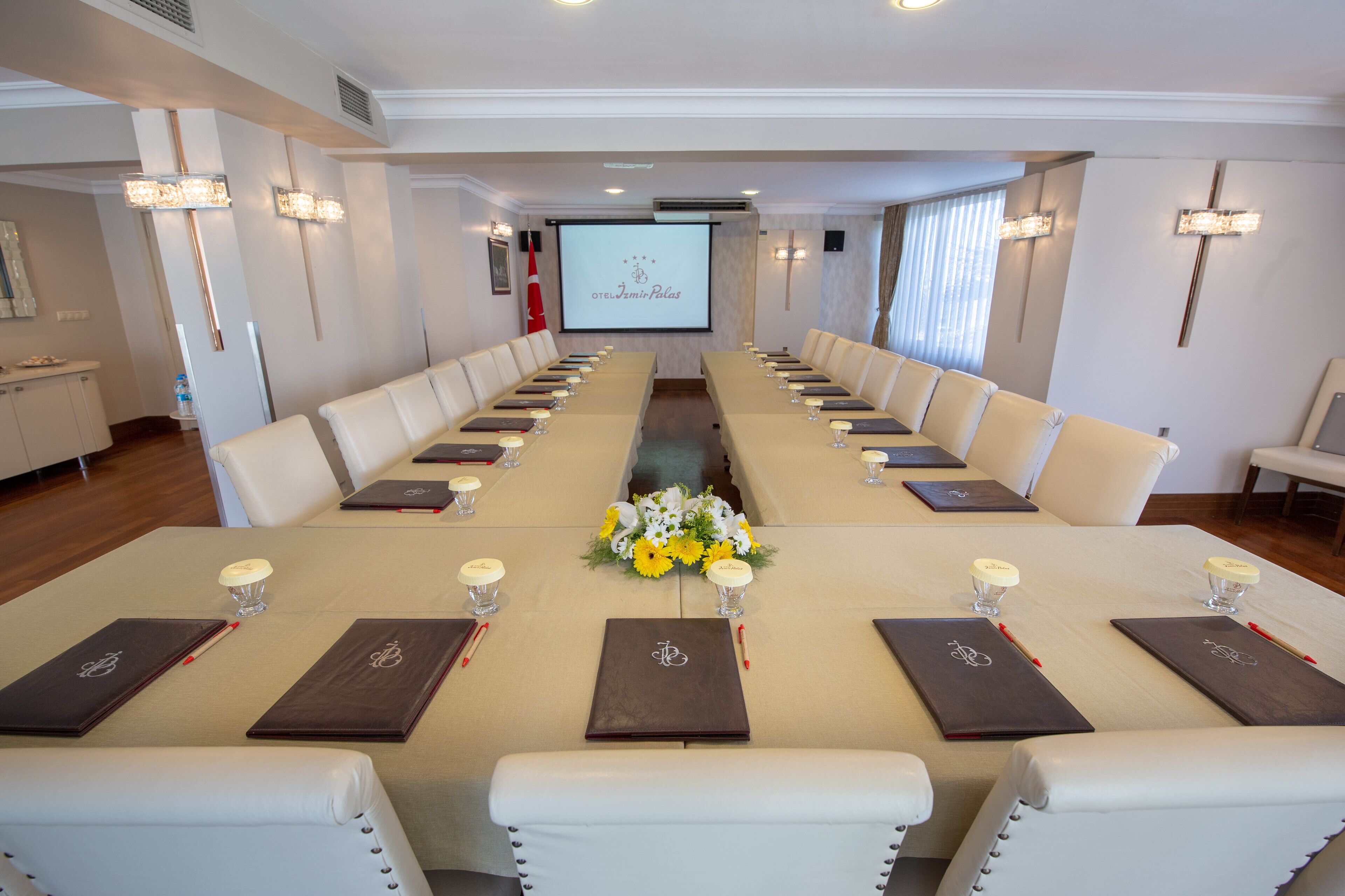 A conference room with a long table, white chairs, and a projector screen displaying a logo.
