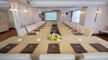 A conference room with a long table, white chairs, and a projector screen displaying a logo.