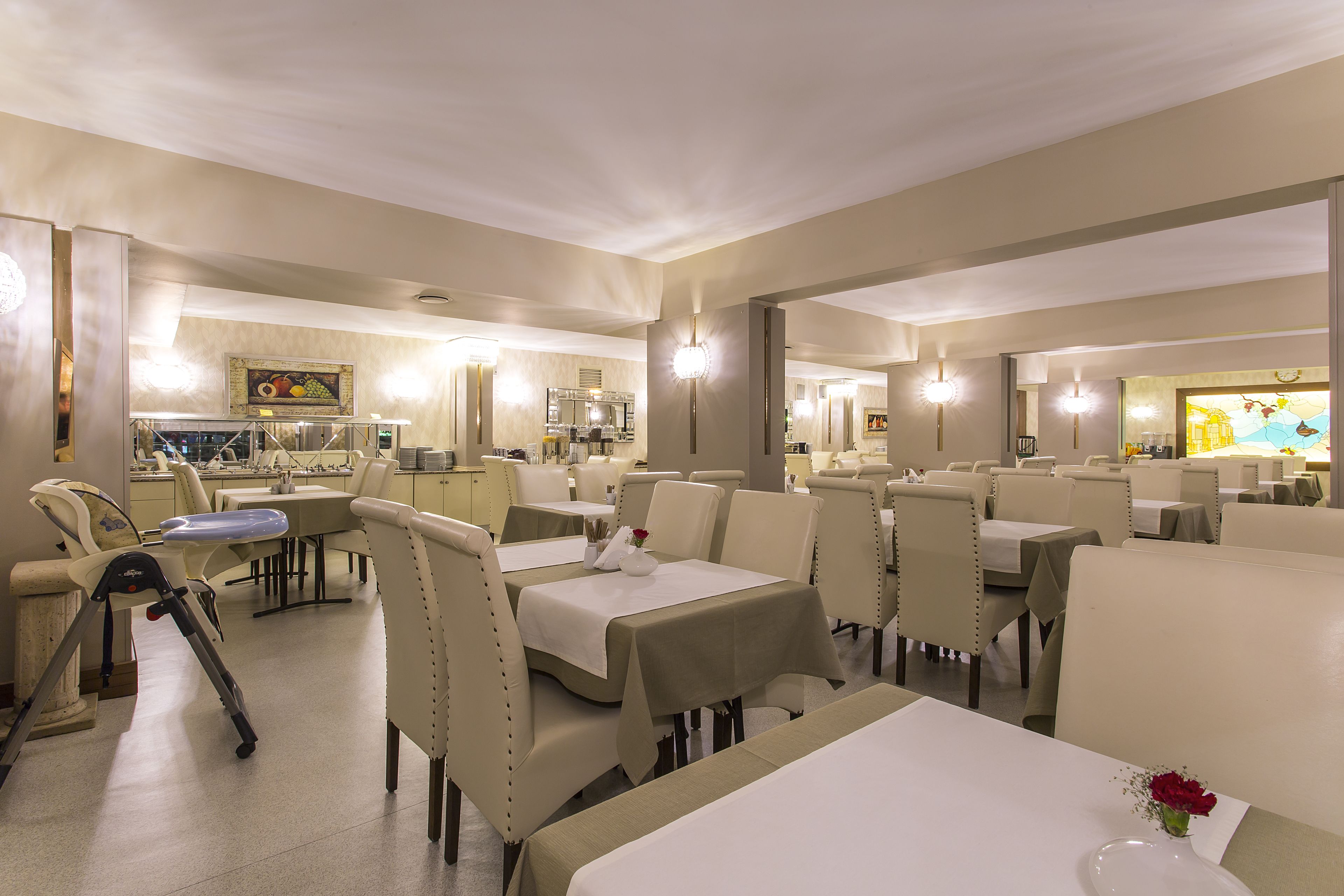 Un restaurante con varias mesas y sillas, una zona de comedor y una cocina al fondo.