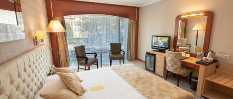 Habitación de hotel con una cama grande, un escritorio, una silla, un televisor y una ventana con cortinas.